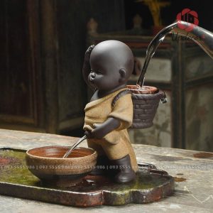 Hình ảnh tượng em bé đứng tiểu màu vàng đang được rót nước từ chiếc giỏ sau lưng rất sống động