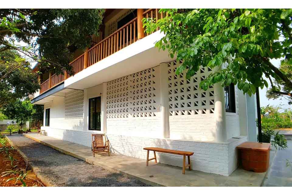 Mặt đứng tầng trệt Giang House với mảng tường gạch bông gió sơn trắng, hiên sâu, lan can gỗ tầng 2 và hàng cây rợp bóng – mẫu biệt thự nhà vườn 2 tầng thoáng mát có hồ bơi