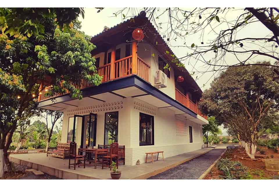 Một góc Giang House Homestay với mái dốc truyền thống, ban công gỗ chạy dài tầng 2, hiên rộng tầng trệt và không gian sân vườn bao quanh – mẫu biệt thự nhà vườn 2 tầng có hồ bơi tại Hòa Bình