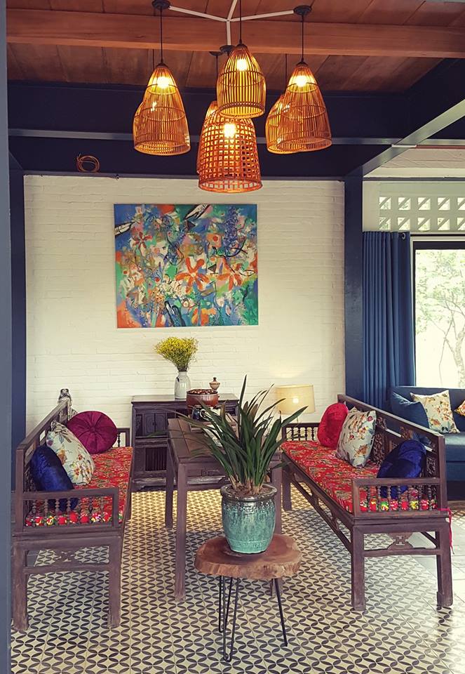 Góc tiếp khách Giang House: cụm đèn mây tre thả trần, tường gạch sơn trắng, bộ trường kỷ gỗ đệm thổ cẩm, chậu cây trên bàn gỗ mộc và sàn gạch bông họa tiết – phong cách nhà vườn hiện đại ấm áp