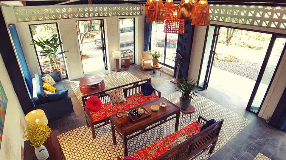 Phòng khách Giang House trần cao, dải gạch bông gió sát trần, cửa trượt kính mở rộng ra vườn; bộ bàn ghế gỗ đệm thổ cẩm, đèn mây tre thả trần và “thảm” gạch bông phân vùng không gian