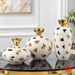 Ba kiểu dáng bình hoa gốm sứ trắng vàng gồm bình cao, bình tròn và bình thấp trên bàn đá đen
