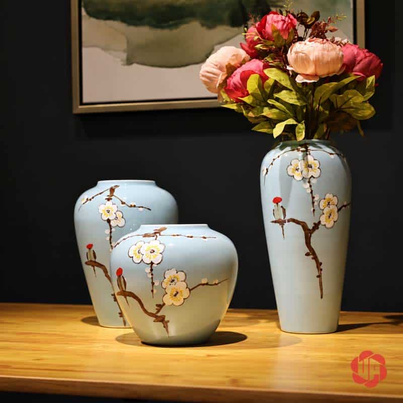 Bộ Bình Gốm Sứ Hoa Mai Trắng 3 Món Trang Trí Phòng Khách BG023 Bộ bình gốm sứ hoa mai trắng xanh ngọc trên bàn gỗ, bình cao cắm bó hoa màu hồng và kem.