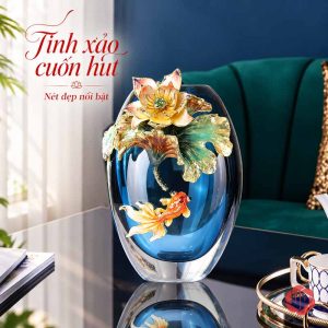 Bình pha lê dáng thấp màu xanh lam với hoa sen nổi và một họa tiết cá màu cam, cạnh ghế xanh