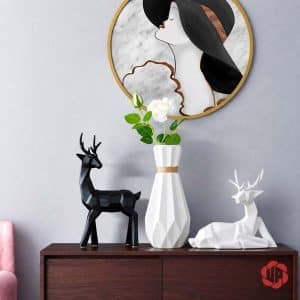 Bình hoa sứ trắng đa giác cắm hoa hồng trắng, đặt giữa tượng hươu đen đứng và hươu trắng nằm.