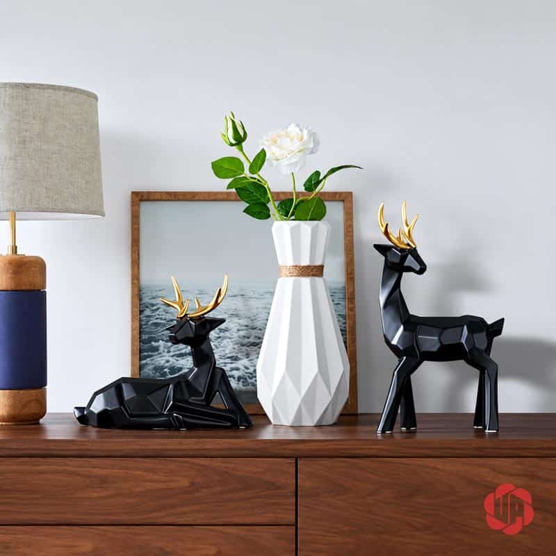 Bộ Tượng Hươu Decor Và Bình Hoa Sứ 3 Món Trang Trí Phòng Khách BG036 Bộ decor gồm hai tượng hươu đen gạc vàng và bình hoa trắng đa giác trên tủ gỗ cạnh đèn và tranh.