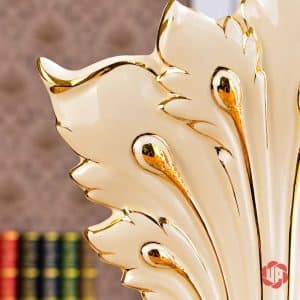 Chi tiết những đường viền ánh vàng trên phần thân uốn lượn của bình hoa chim công trắng.