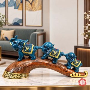 Tượng ba chú voi xanh nối đuôi trên đế cong màu nâu, đặt trên bàn sáng trong phòng khách