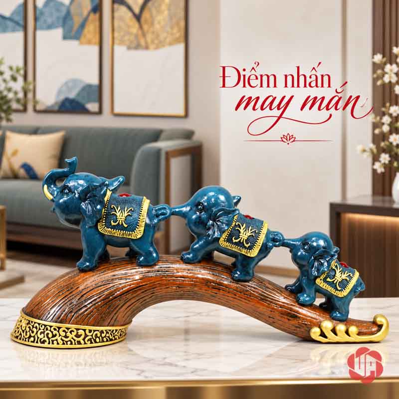 Tượng Gia Đình Voi Hạnh Phúc Trang Trí Nội Thất Phòng Khách UPV022 Ba chú voi xanh nối đuôi trên đế cong nâu, phía sau là sofa và tủ gỗ